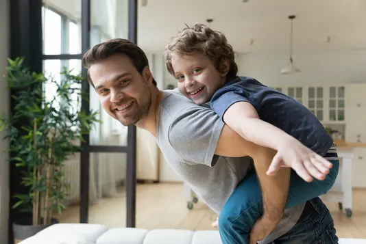 Haus-Familie-Wohnen-Serie-3-20 Vater mit Sohn auf dem Rücken im Wohnzimmer