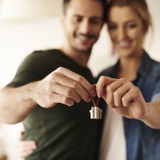 Paar vor dem eigenen Haus als Symbol für die Bauvoranfrage. Klärung der Genehmigungsfähigkeit vor Grundstückskauf spart Zeit und Kosten.